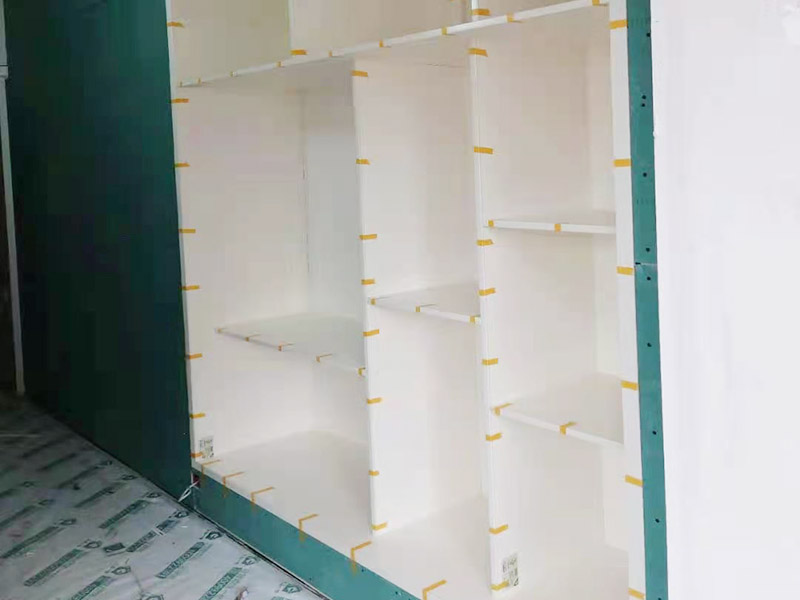 客廳定制柜體安裝：用墊布點好地板，先從靠墻的一端寬側板開始組裝，將寬側板平放于地面上（離后墻面保持700mm間隔）。首先將填好的三合一膠塞的板件，平放在墊布上，檢查孔距與圖紙相符，并裝上三合一單連桿。然后將固層釘上木塞，固定于寬側板上面，頂板大柄孔朝上，其余固層都朝下，腳線大柄孔朝內（中間固層與L架高度一致，即底板到固層內空為960mm，現場打層板孔）。放上側板，釘上木塞，木塞要求連通兩邊的固層。在第二個柜固層上面裝好雙連桿，留意雙連桿上面大柄只能鎖住一半，即90°。當兩件固層與側板固定后再同時擰緊大柄。裝第三個柜時重復第二個柜的安裝步驟。